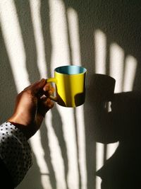 Midsection of person holding coffee cup against wall