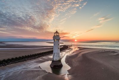 Lighthouse by sea against sky during sunset