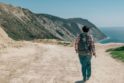 An adult woman with a backpack and in a plaid shirt went hiking in the mountains near the ocean