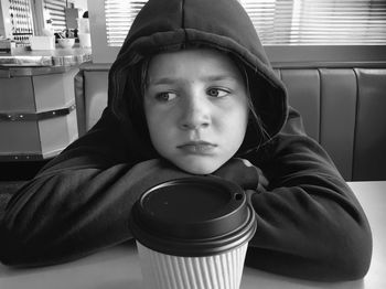 Boy looking away while leaning on table in cafe