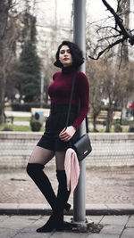 Portrait of young woman standing against pole in city