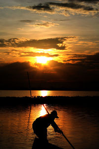 Silhouette man standing in sea against sky during sunset