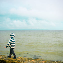 Child walking on retaining wall against sea