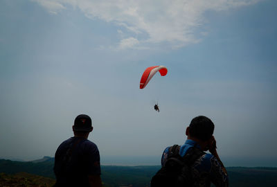 Rear view of people paragliding against sky