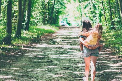 Rear view of mother piggybacking daughter while walking in forest