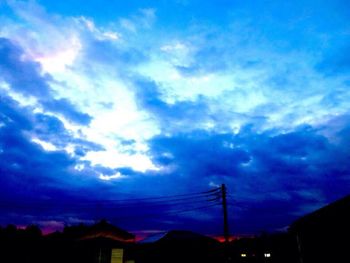 Low angle view of silhouette electricity pylon against dramatic sky