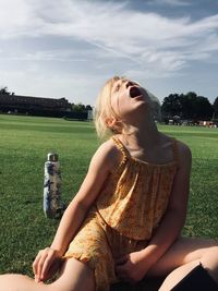 Young woman sitting on field against sky