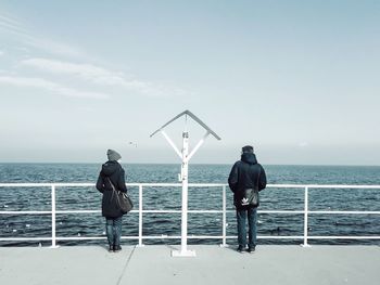 Rear view of man and woman standing on promenade by sea against sky