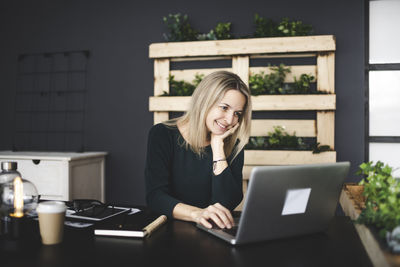 Smiling young woman using phone on table