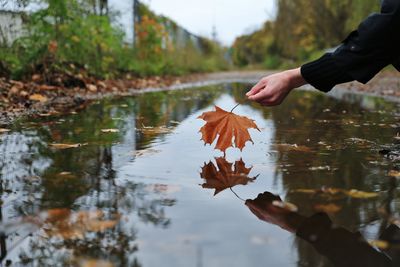 Reflection of person holding autumn leaves in lake