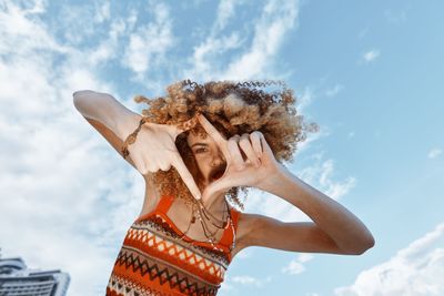 Low angle view of woman with arms raised against sky