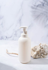 A minimalistic scene of a podium and white dispenser bottle with stones on white background