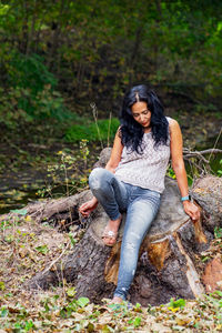 Portrait of young woman sitting on wood in forest