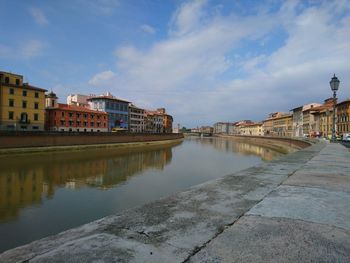 View of buildings by river against cloudy sky