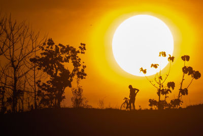 Silhouette trees on field against orange sky