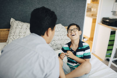 Laughing disabled boy sitting with father on bed at home