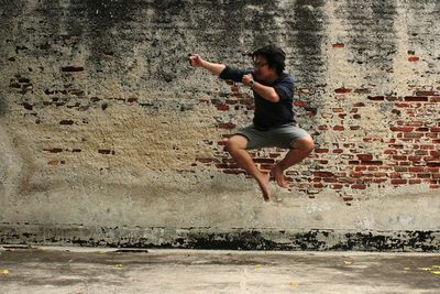 Man gesturing while jumping against old brick wall