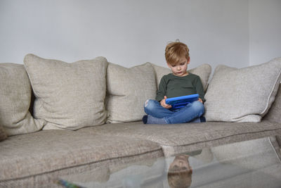 Boy sitting on sofa at home and playing tablet