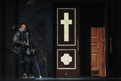 Man with walking cane leaning outside house