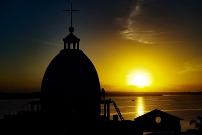 Silhouette built structure by sea against orange sky