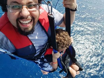 Portrait of smiling father parasailing with son over sea