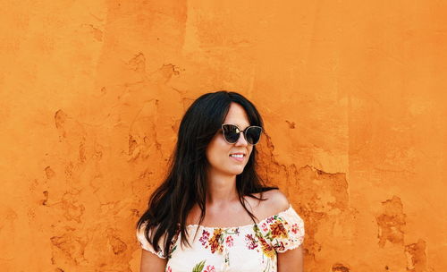 Beautiful young woman standing in front of weathered orange wall. happy, smiling, lifestyle.