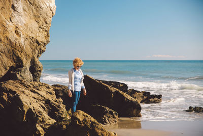 Woman standing on rock by sea against sky