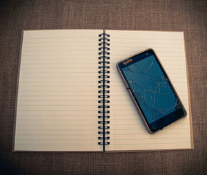 High angle view of smart phone with spiral notebook on table