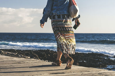 Low section of woman on pier over sea against sky