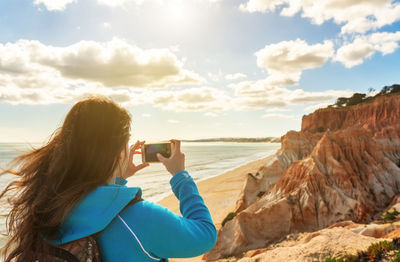 Woman photographing sea against sky