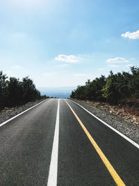 Empty road by trees against sky