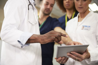 Doctor gesturing near colleagues using tablet pc in meeting at hospital