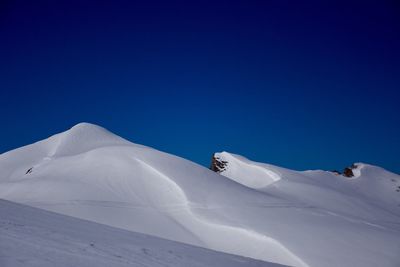 Snow covered landscape against clear blue sky