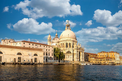 Buildings by river against cloudy sky