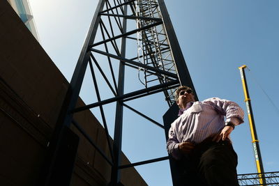 Low angle view of man standing on ladder against sky