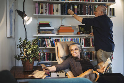 Senior woman taking selfie while man arranging books on shelf