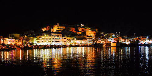 Illuminated city by sea against clear sky at night