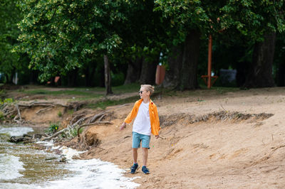 A boy in an orange shirt on the seashore. a child in sunglasses person