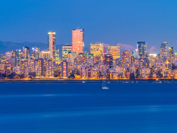 Illuminated buildings in city against clear blue sky