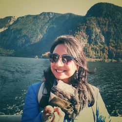 Portrait of smiling young woman standing by lake against mountains