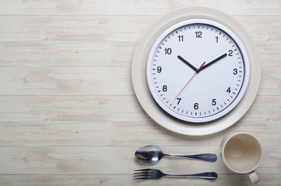 Directly above shot of wall clock in plate by cutlery on table