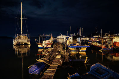 Sailboats moored at harbor against sky at night