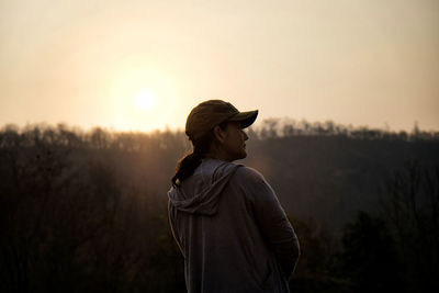 Woman looking away while standing against sky during sunset