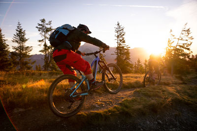 2 adults riding their mountain bikes in early morning light on footpath, lens flare, backlight