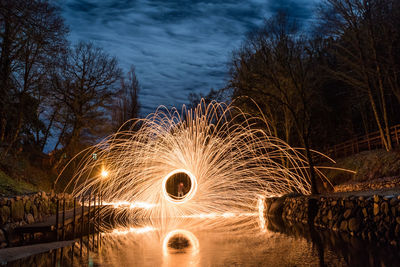 Blurred motion of illuminated trees by river against sky at night