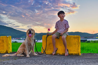 Boy with dog sitting against sky during sunset