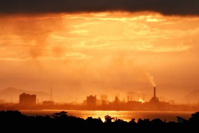 Silhouette of factory against sky during sunset