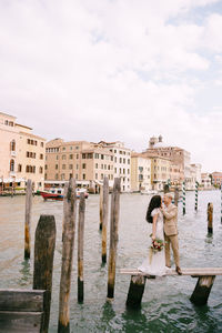 Women standing by canal against sky in city