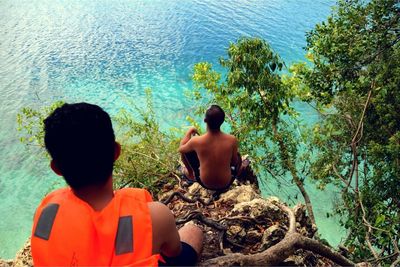 Rear view of shirtless boy sitting in water against trees