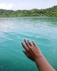 Close-up of hand by sea against sky